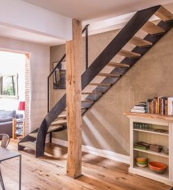 Escalier avec bibliothèque intégrée et un meuble sur mesure formant les premières marches. Escalier avec double limon métal patiné et bois chêne lamellé collé.