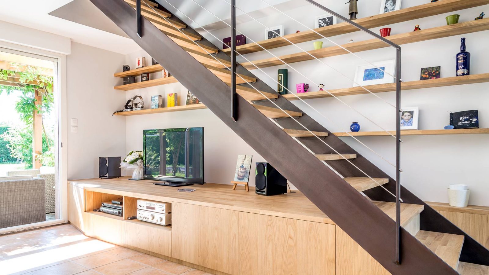 Escalier avec bibliothèque intégrée et un meuble sur mesure formant les premières marches. Escalier avec double limon métal patiné et bois chêne lamellé collé.